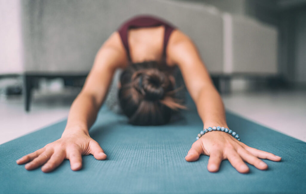 Woman stretching at home in Child’s Pose to reduce soreness after lifting weights